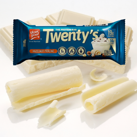 Una imagen de un "Praliné de Avellanas Barras De Proteina Twenty 12un" de YOUR GOAL empaquetado en un envoltorio azul. La barra contiene 19 g de proteína y 1 g de azúcar, perfecta para personas con metas físicas. Virutas y bloques de chocolate blanco están ingeniosamente dispuestos alrededor de la barra.